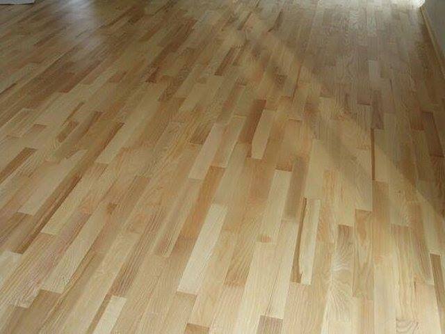 Świeżo położona, jasna podłoga z parkietu drewnianego, ułożona w klasyczny wzór, widoczna z niskiego kąta, z delikatnym połyskiem.