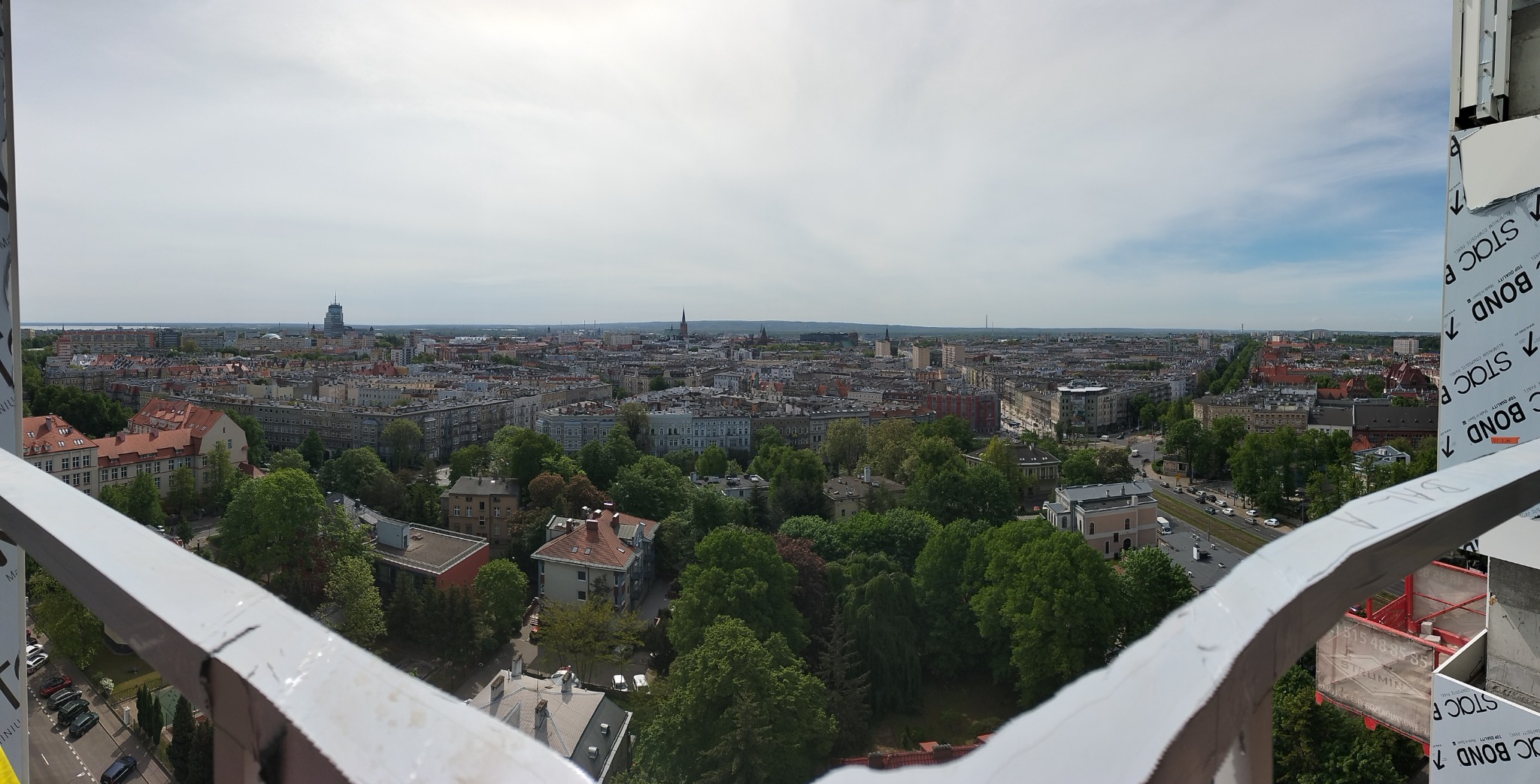 Panorama miasta z wysokości, widok z balkonu w trakcie montażu, widoczne elementy konstrukcyjne balkonu z panelami STACBOND.