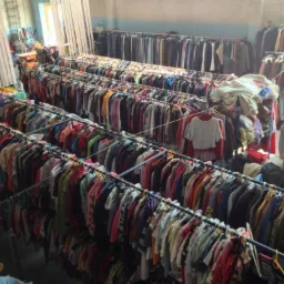 Hala z rzędami wieszaków pełnych różnorodnych ubrań używanych, widok z góry, z jasnym oknem w tle. Selekcja odzieży, hurtowe ilości.