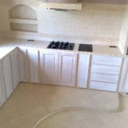 Jasna kuchnia z białymi szafkami, płytkami i okapem w Głogowie, widok na płytę grzewczą i fragment podłogi z dekoracyjnym obramowaniem.