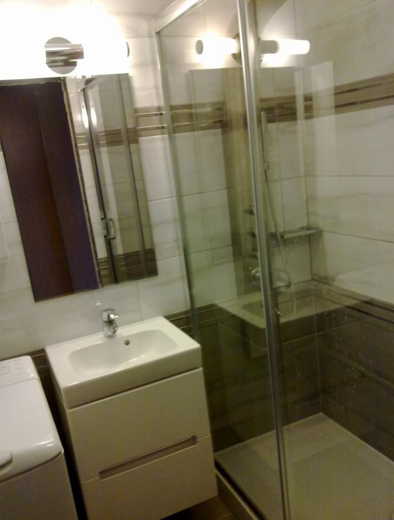 Nowoczesna łazienka z kabiną prysznicową, umywalką z szafką i pralką, oświetlona światłem halogenowym.