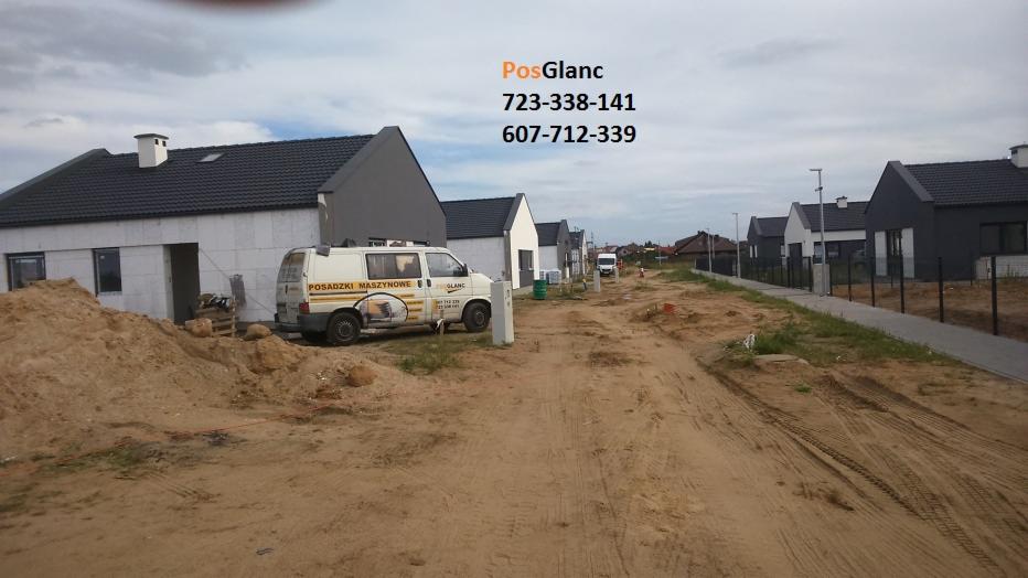 Flota firmy PosGlanc z Tuliszkowa na placu budowy domów jednorodzinnych. Na samochodzie reklama posadzek maszynowych. Droga gruntowa, w tle zabudowa szeregowa.