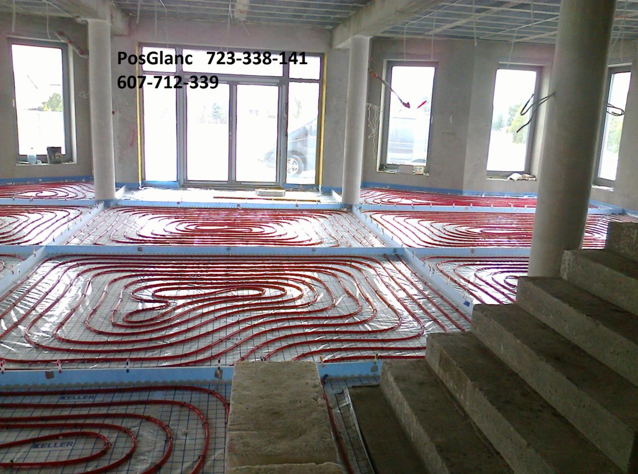 Czerwone rury ogrzewania podłogowego ułożone na izolacji w nowym budynku, widoczne schody i okna. Etap przed wylewką.