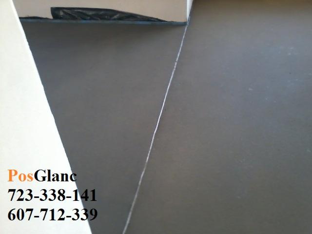 Gładka, szara posadzka po wylewce, widoczna linia dylatacyjna przy ścianie. Ujęcie z bliska, prezentujące równą powierzchnię i wykończenie podłogi.