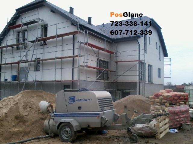 Sprężarka DMS Worker N1 na tle domu w rusztowaniach, przygotowana do wylewki posadzki. Widoczne worki z materiałem i hałda piasku.