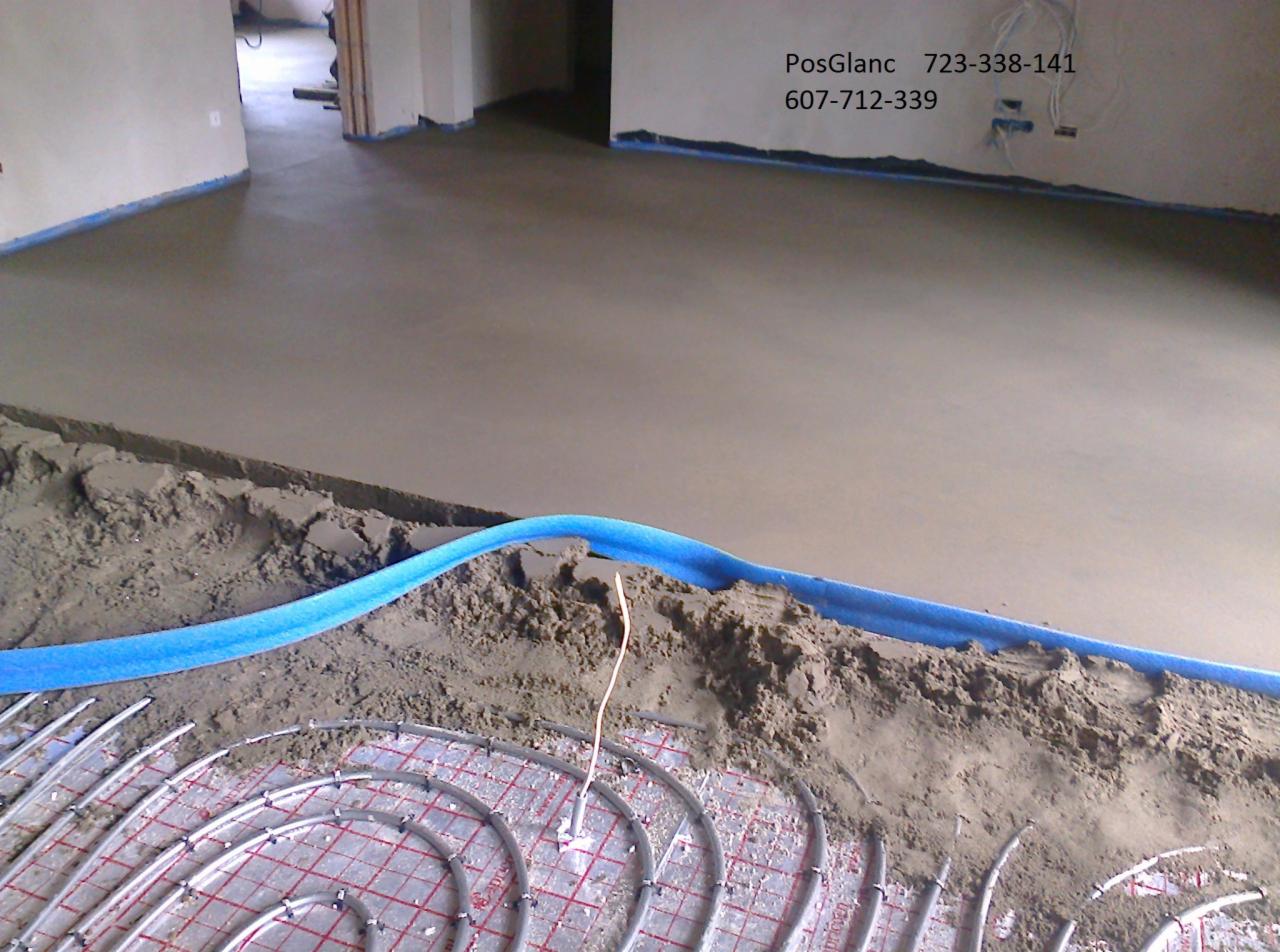 Wylewka podłogowa w trakcie realizacji: widoczne rury ogrzewania podłogowego przed zalaniem, oddzielone niebieską izolacją. W tle gładka, świeżo wylana posadzka.