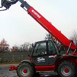 Czerwony wózek teleskopowy Manitou na placu budowy, widok z dołu, pochmurne niebo w tle.