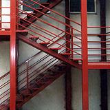 Czerwona, metalowa konstrukcja schodów w budynku w Sieradzu, z widocznymi spawami i elementami mocującymi.