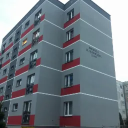 Odnowiony blok mieszkalny w szaro-czerwonej kolorystyce z widocznym napisem 'SM WOLA UL. SŁONECZNA 2-4-6' na elewacji.