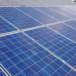 Panele słoneczne z widoczną strukturą krzemu na dachu pokrytym szarą dachówką ceramiczną.