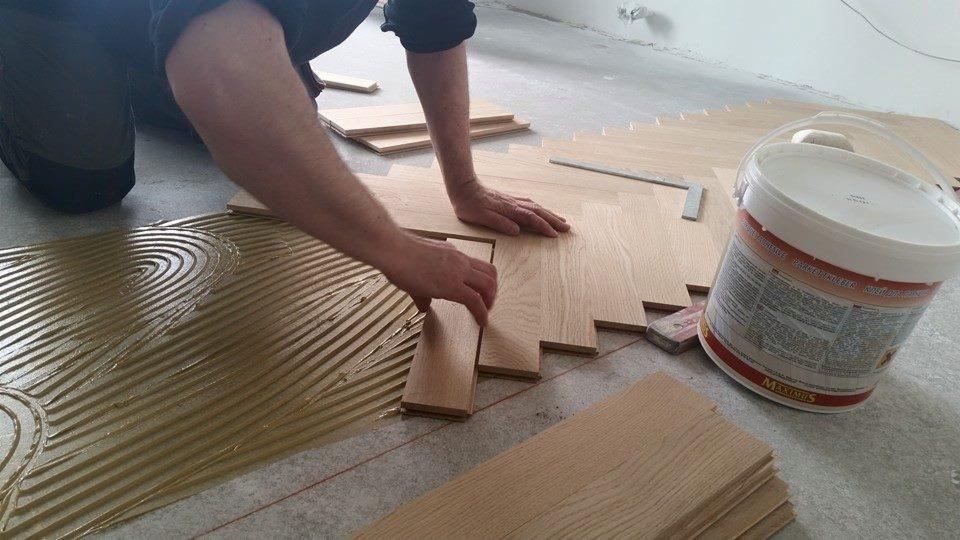 Montaż drewnianej podłogi w Kielcach: parkiet układany na klej, widoczny wzór rozprowadzonego kleju i narzędzia pracy.