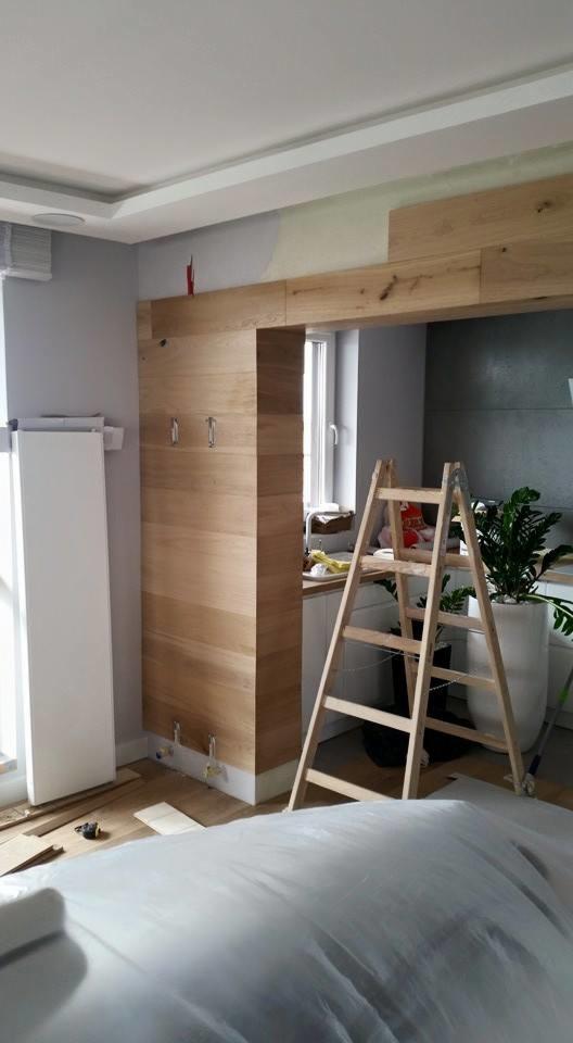 Montaż drewnianej obudowy przejścia w mieszkaniu, widoczna drabina i zabezpieczona folią podłoga w trakcie prac wykończeniowych.