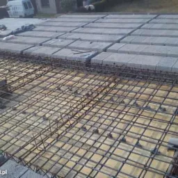 Zbrojenie stropu Teriva z betonowymi pustakami, widok z góry. Siatka z prętów stalowych tworzy regularną strukturę na deskowaniu.