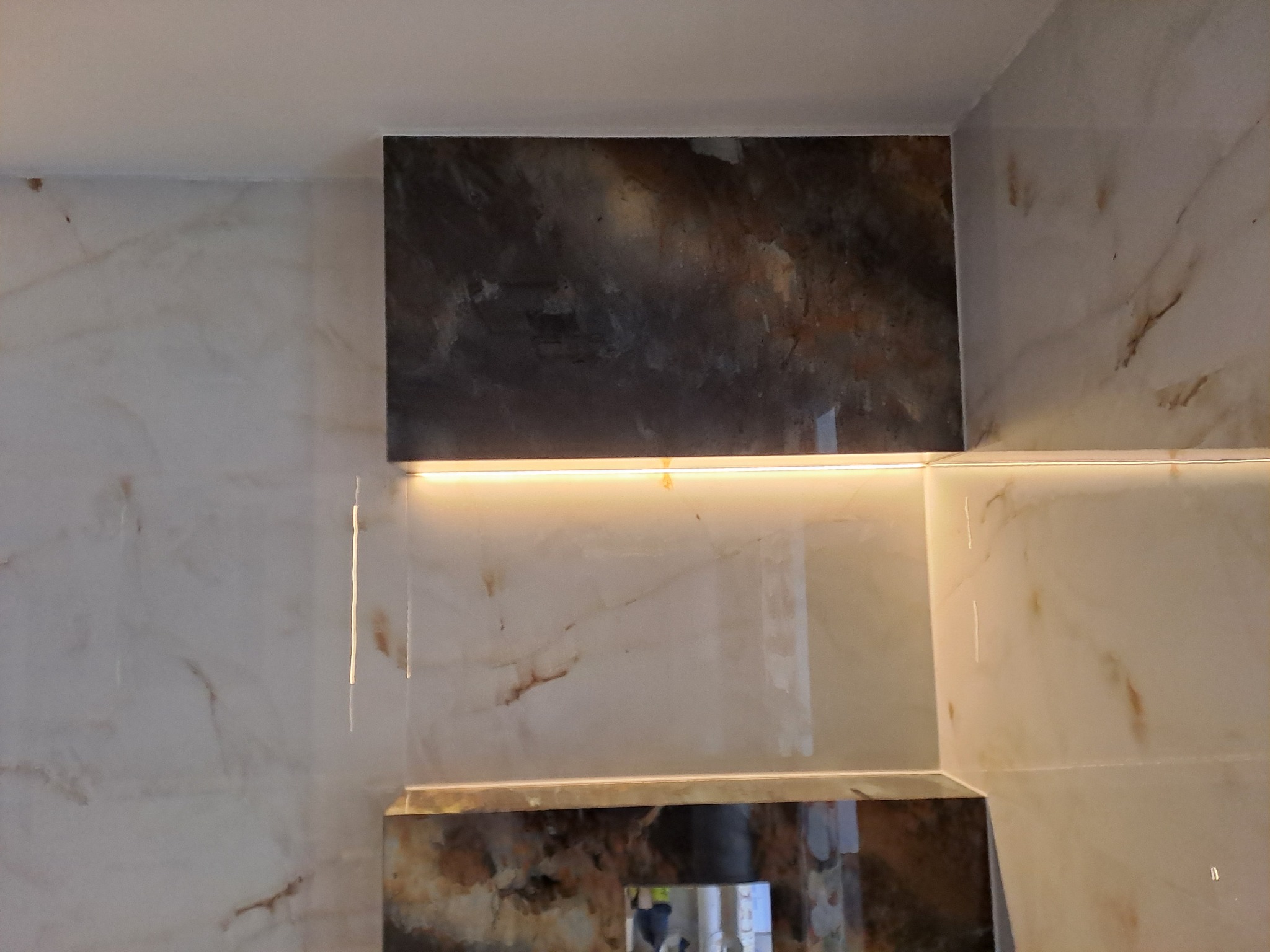 Fragment ściany łazienki wyłożonej jasnymi, marmurkowymi płytkami z ciemnymi wstawkami i podświetleniem LED w szczelinach.