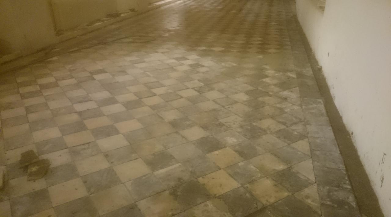 Ułożona podłoga z kwadratowych płytek w szachownicę, widoczne ślady zaprawy przy ścianie, co sugeruje świeżo zakończone prace.
