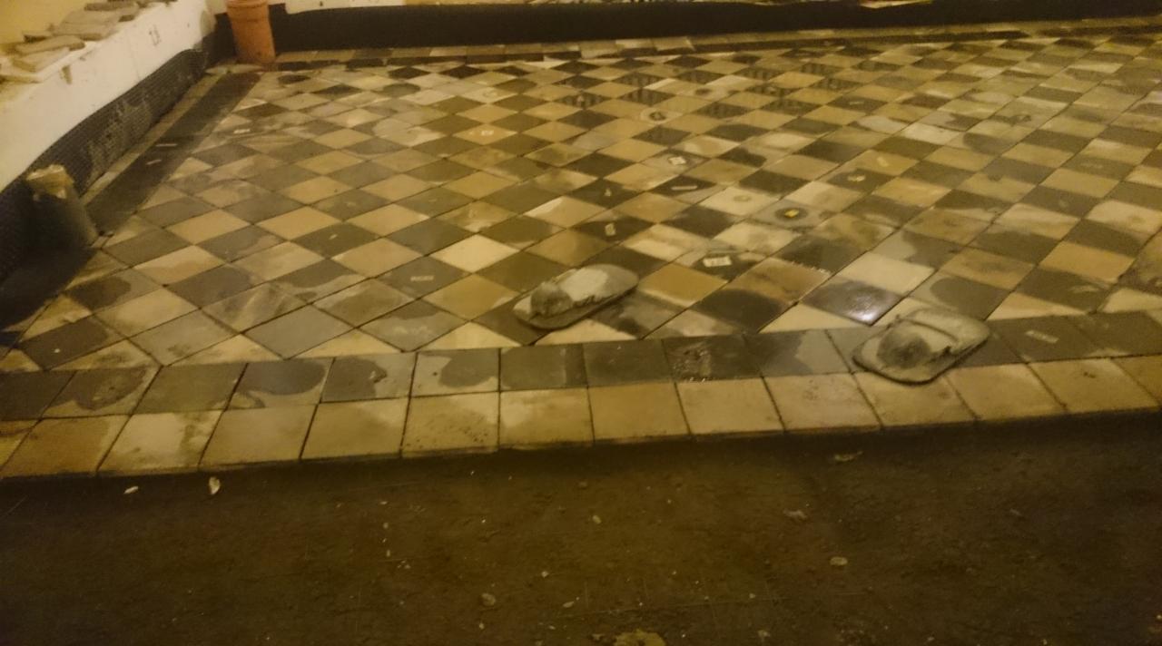 Układanie podłogi z płytek w szachownicę. Widoczne narzędzia glazurnicze. Częściowo ułożona podłoga w pomieszczeniu. Praca w toku, z bliska.