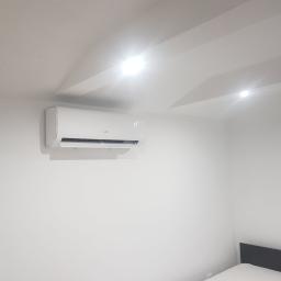 C.L.Klima - Biały klimatyzator ścienny marki MDJ zamontowany w jasnym pokoju z widoczną temperaturą 22 stopnie Celsjusza na wyświetlaczu.