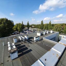 C.L.Klima - Widok z góry na płaski dach budynku komercyjnego z zainstalowanymi jednostkami klimatyzacyjnymi i wentylacyjnymi, w tle parking i zieleń miejska pod błękitnym niebem.