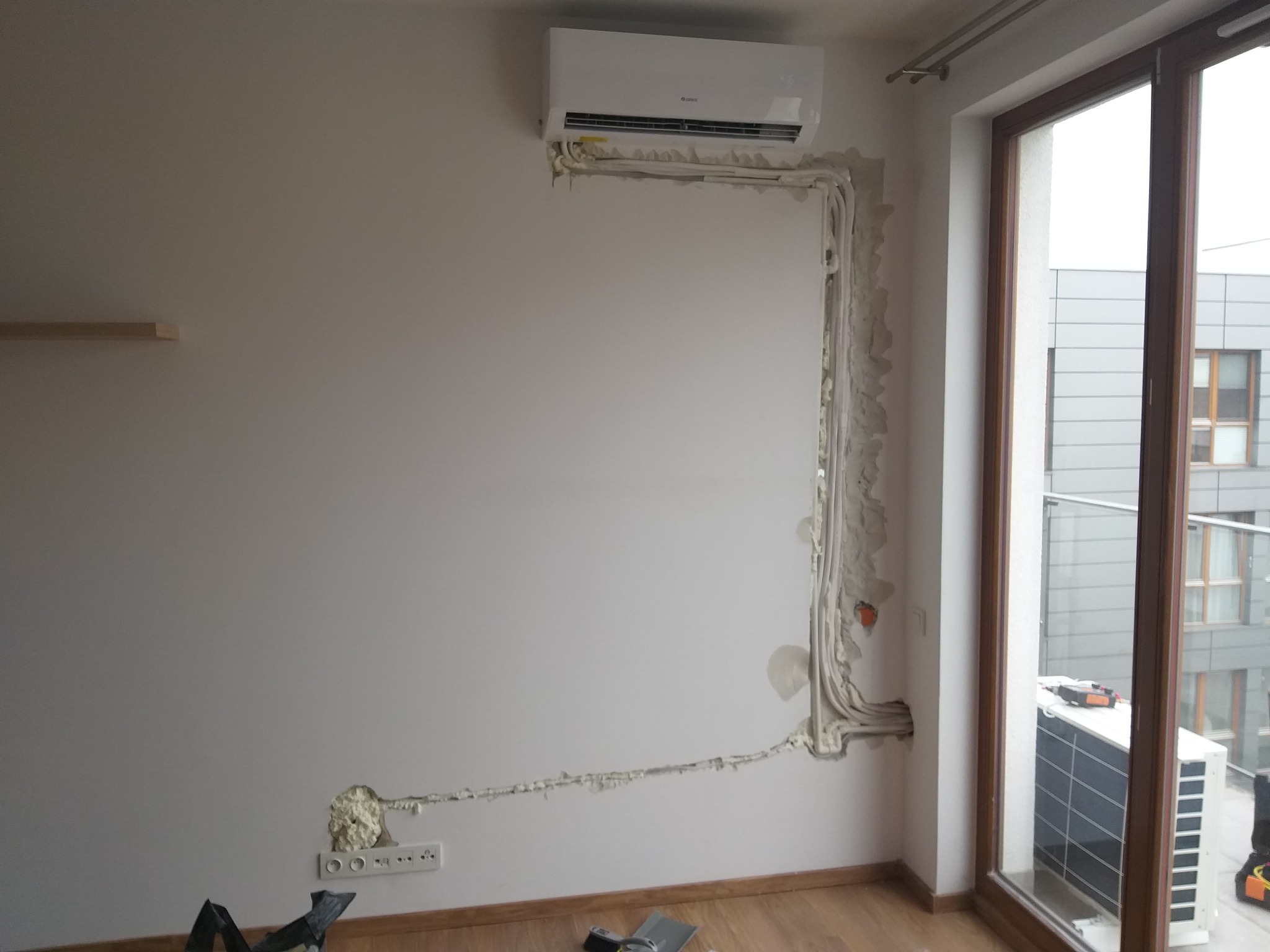 Montaż klimatyzatora Gree w mieszkaniu, widoczne rury i przewody zabezpieczone pianką montażową, jednostka zewnętrzna widoczna przez okno.