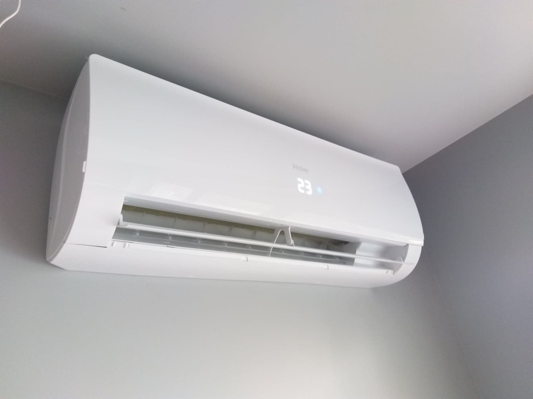 Biała jednostka klimatyzacji Haier zamontowana na ścianie; widoczny wyświetlacz z temperaturą 23 stopnie.