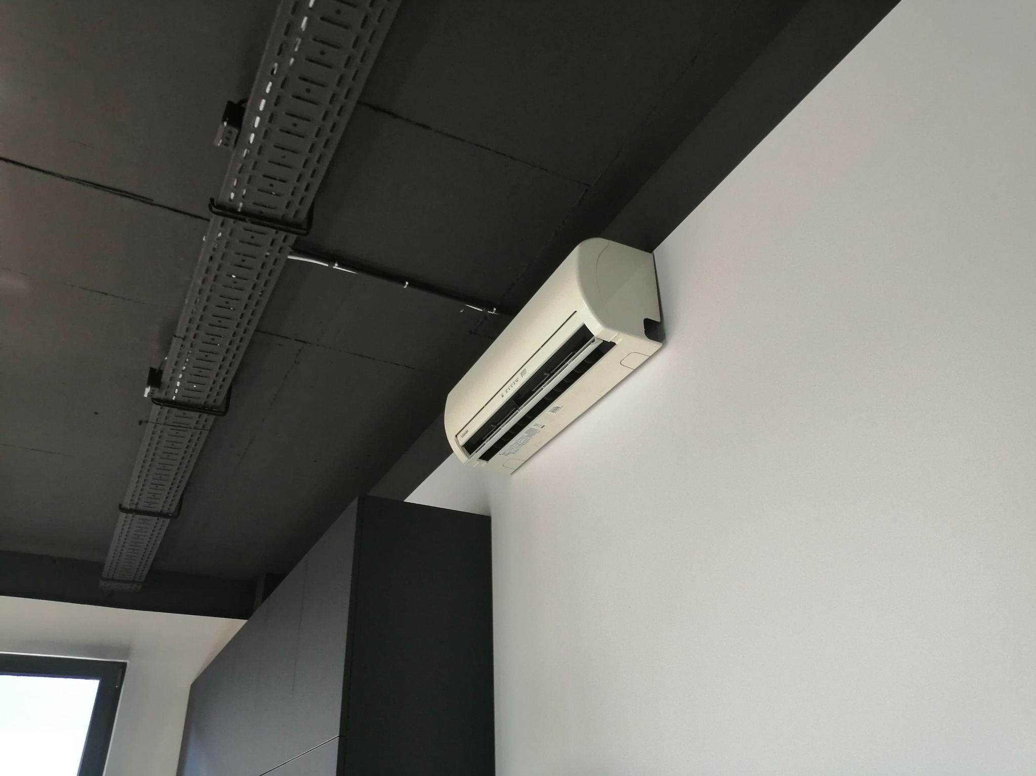 Biała klimatyzacja ścienna w nowoczesnym biurze z czarnym sufitem i szynami kablowymi