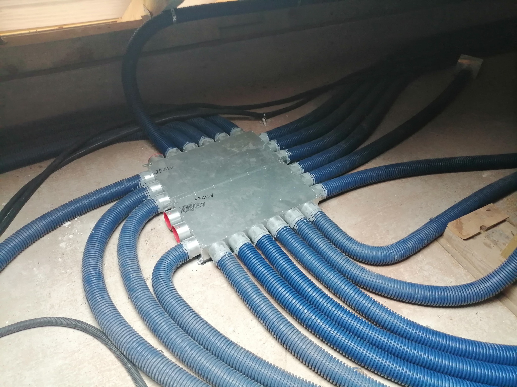 Rozdzielacz wentylacyjny z podłączonymi elastycznymi przewodami wentylacyjnymi w kolorze niebieskim, widoczne napisy na obudowie rozdzielacza.