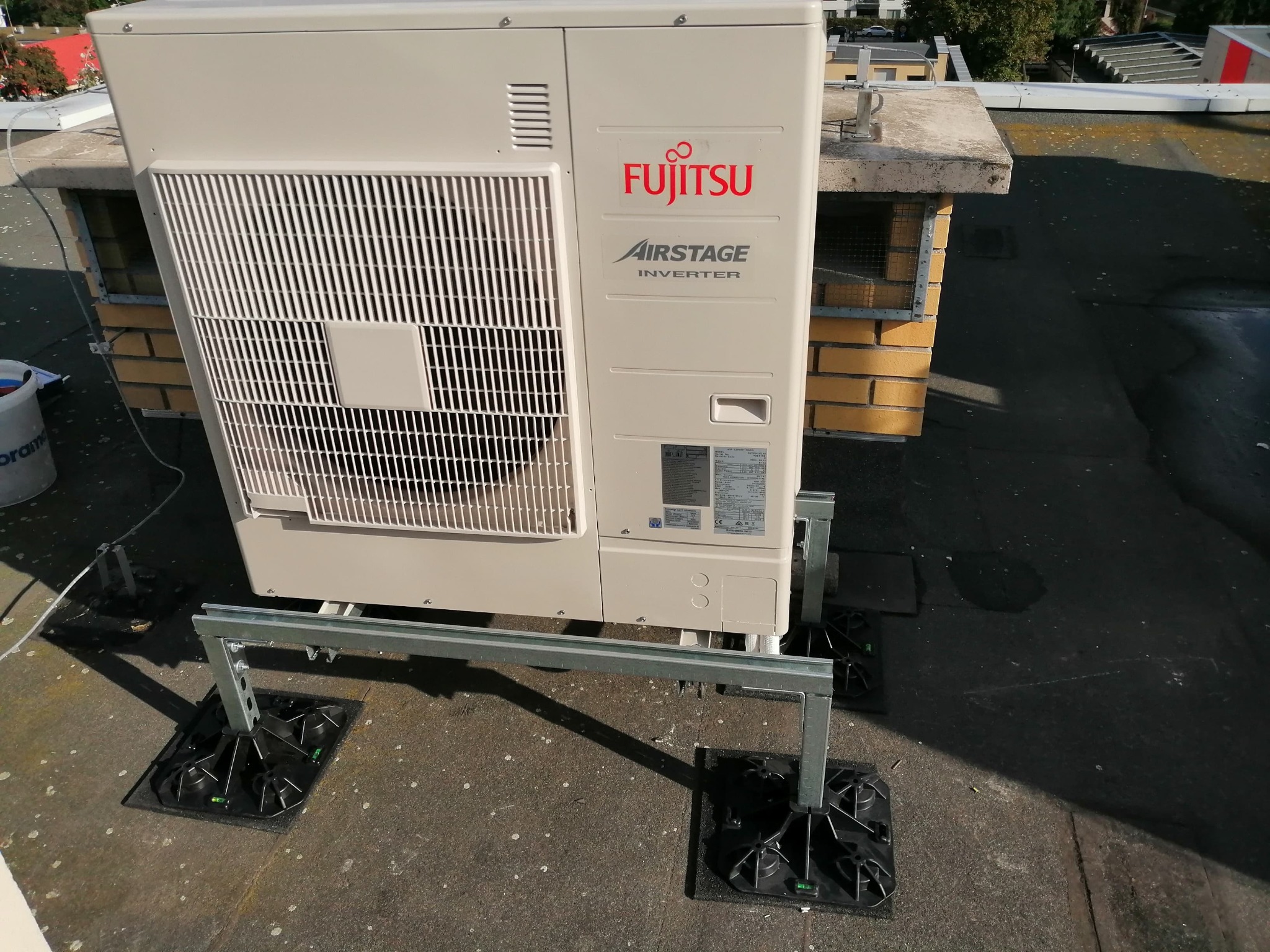 Zewnętrzna jednostka klimatyzacyjna Fujitsu Airstage Inverter zamontowana na dachu budynku, widoczne elementy konstrukcji wsporczej i czarne podstawy antywibracyjne.