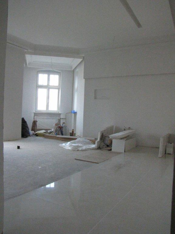 Wykończone pomieszczenie z błyszczącą posadzką, widoczne materiały budowlane i okno w tle.