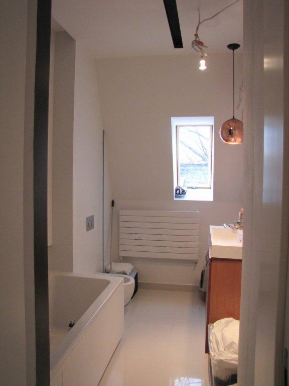 Jasna łazienka po remoncie z wanną, grzejnikiem drabinkowym, oknem dachowym i miedzianą lampą wiszącą