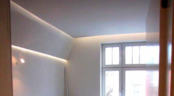 Wykończone wnętrze po remoncie: białe ściany z ukrytym oświetleniem LED, białe okno skrzynkowe z widokiem na zewnątrz, fragment drewnianej ramy drzwiowej po prawej stronie.