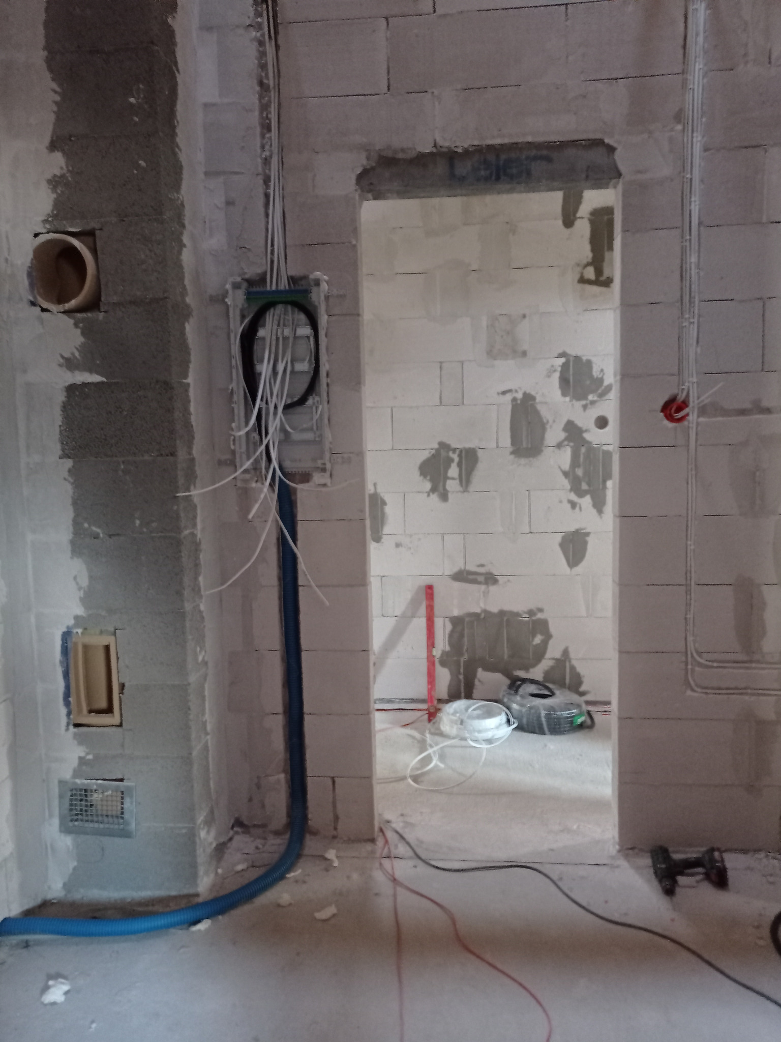 Wnętrze w trakcie prac elektrycznych: kable wychodzące ze ściany, niebieska rura ochronna, puszka instalacyjna, ściany z betonu komórkowego, narzędzia w tle.