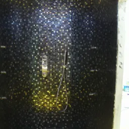 Kabina prysznicowa wykończona mozaiką w odcieniach czerni i złota, z zamontowaną deszczownicą i baterią natryskową, widoczne dysze do hydromasażu.