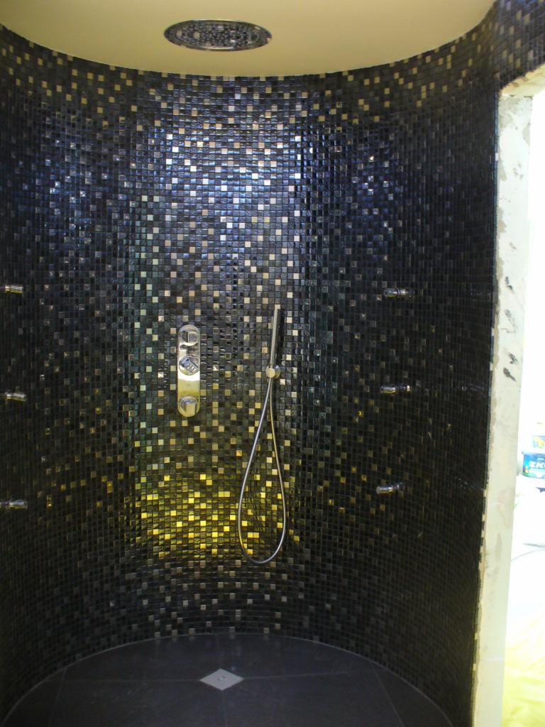 Kabina prysznicowa wykończona mozaiką w odcieniach czerni i złota, z zamontowaną deszczownicą i baterią natryskową, widoczne dysze do hydromasażu.