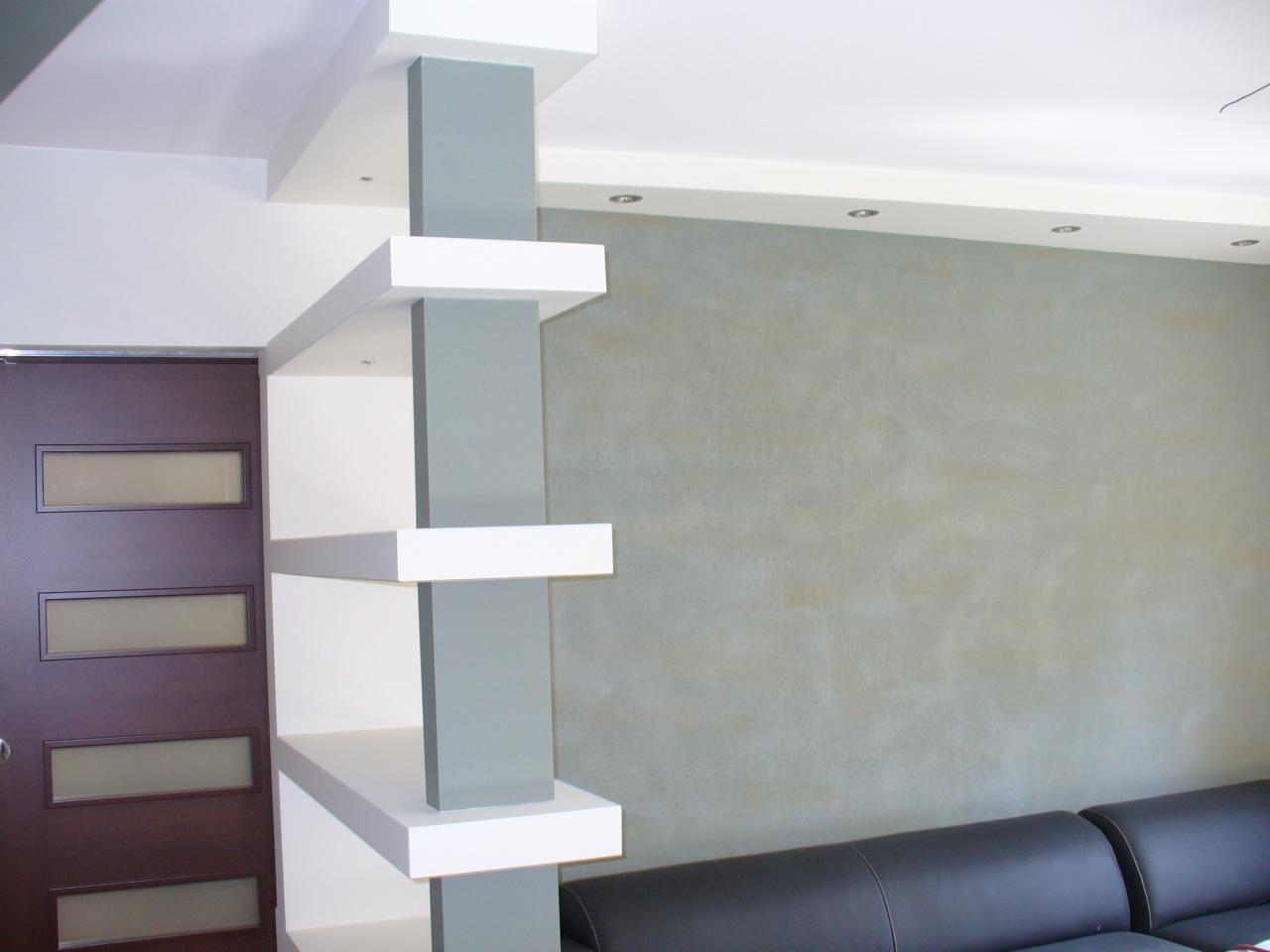 Nowoczesna ściana działowa z półkami w kolorze białym i szarym, oddzielająca przestrzeń w pokoju z brązowymi drzwiami i szarą ścianą.