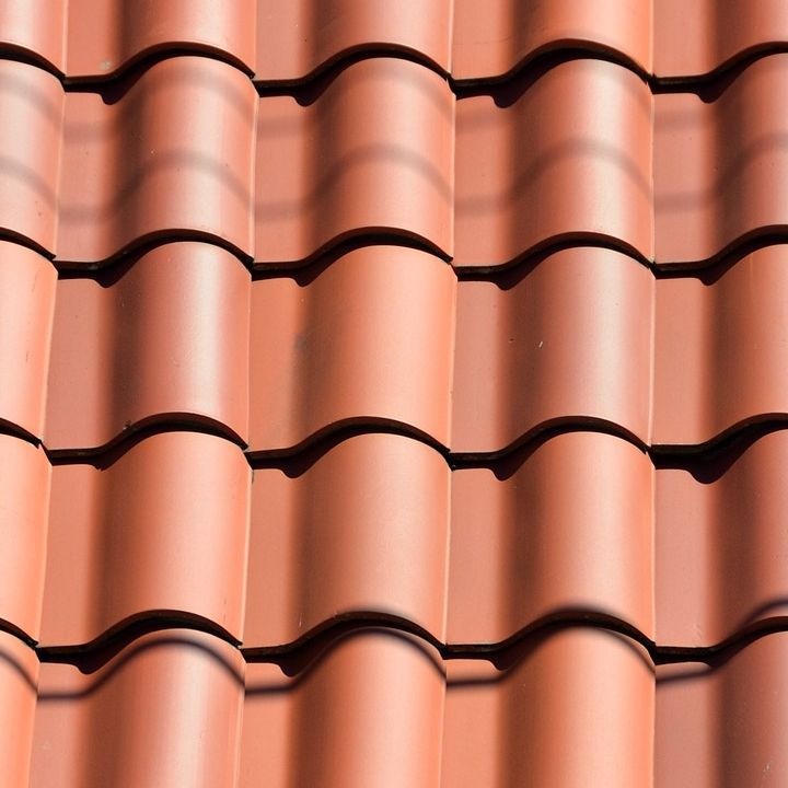 Czerwona dachówka ceramiczna w zbliżeniu, z widocznymi falami i cieniami, tworząca regularny wzór na dachu. Detal pokrycia dachowego w słoneczny dzień.