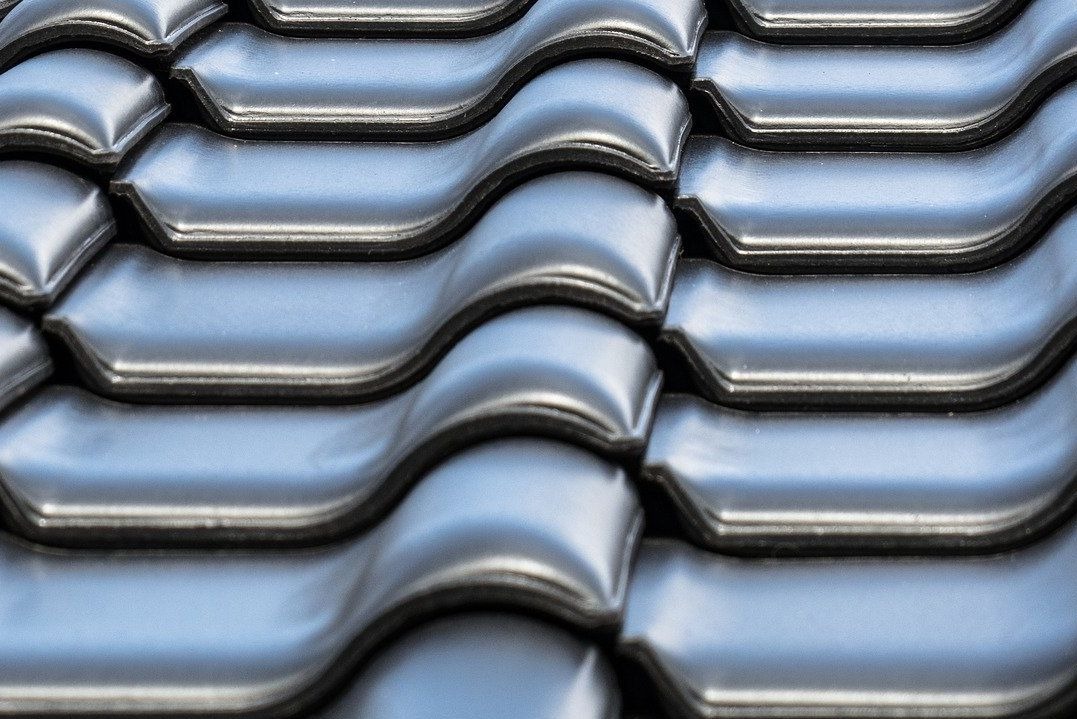 Błyszczące, ciemnoszare dachówki ceramiczne ułożone rzędami, widoczne z bliska, z delikatnym odbiciem światła. Regularny wzór i faktura.