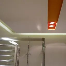 Nowoczesna łazienka z podwieszanym sufitem i oświetleniem LED. Kabina prysznicowa ze szklanymi drzwiami i grzejnik drabinkowy.