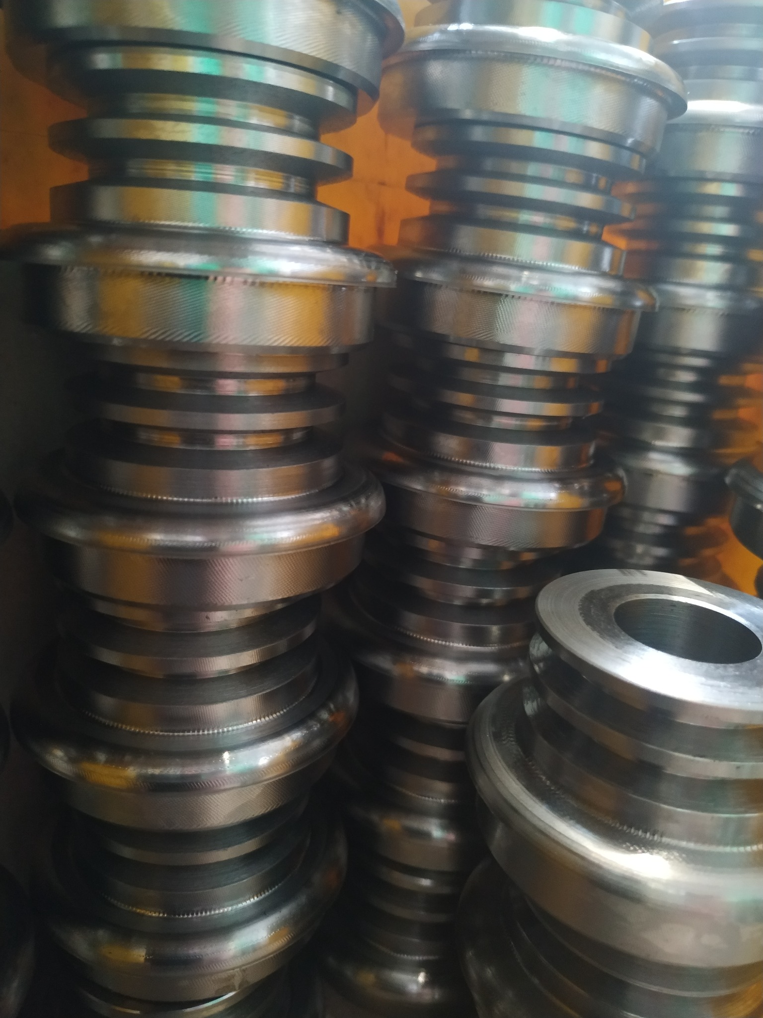 Stos metalowych, precyzyjnie obrobionych elementów z rowkowaną powierzchnią, ułożonych jeden na drugim, z widocznymi śladami obróbki.