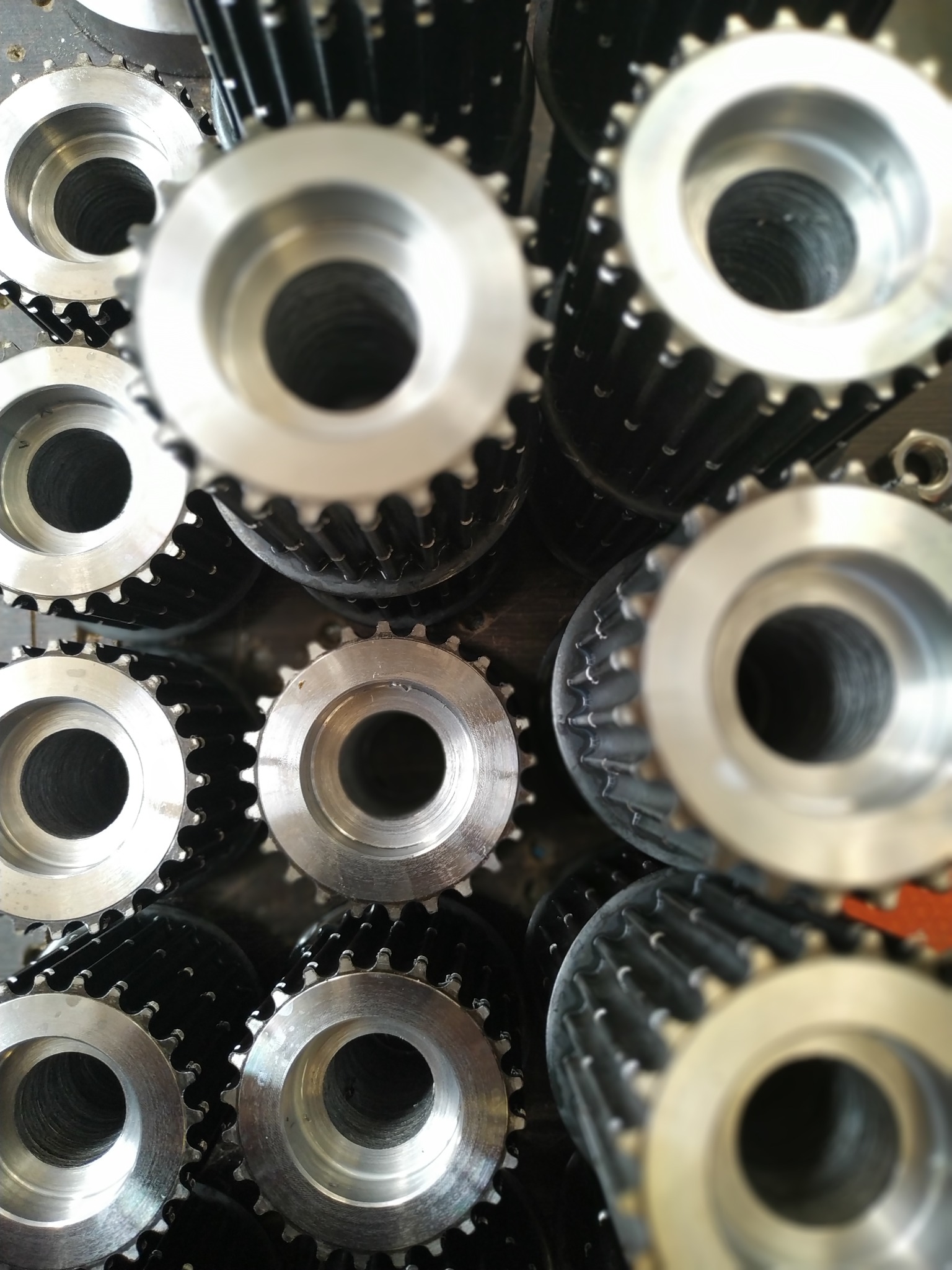 Srebrne, metalowe koła zębate ułożone blisko siebie, widoczne z góry pod kątem. Część kół jest ostra, a część rozmyta, co daje efekt głębi ostrości.