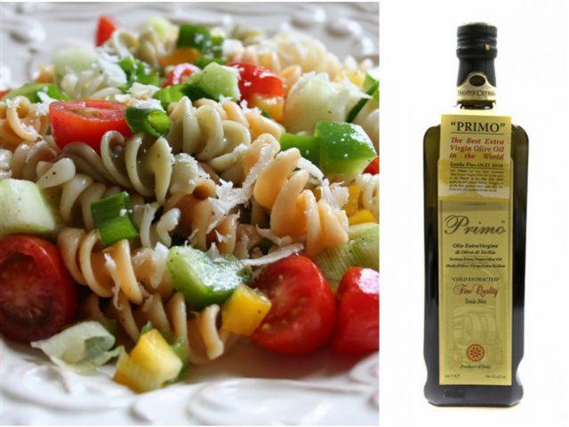 Kolorowa sałatka z makaronem, pomidorami i papryką na talerzu obok butelki oliwy 'Primo', prezentacja składników do cateringu.