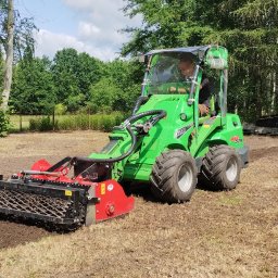 SOSENKA- Adam Wawryło - Zielony traktor Avant 528 z glebogryzarką przygotowuje ziemię pod zasiew na tle drzew i nieba. Widoczny operator w kabinie.