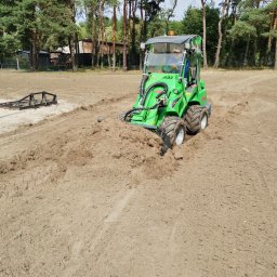 SOSENKA- Adam Wawryło - Zielony miniładowarka Avant 528 wyrównuje teren pod przyszły ogród. W tle drzewa i budynek. Widoczne ślady opon na piasku.