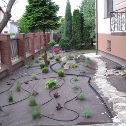 SOSENKA- Adam Wawryło - Nowo założony ogród z rozłożoną agrowłókniną, systemem nawadniania i posadzonymi roślinami. Ścieżka z kamieni prowadzi wzdłuż budynku.