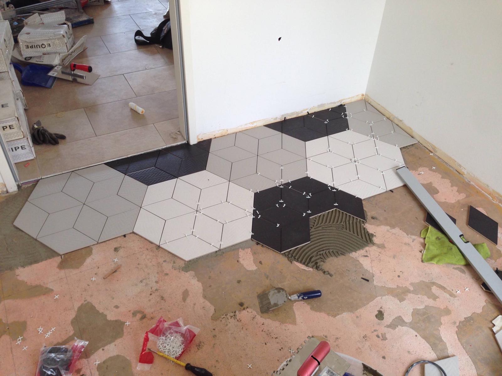 Układanie heksagonalnych płytek w odcieniach szarości, bieli i czerni z efektem 3D, widoczne narzędzia glazurnicze i krzyżyki dystansowe.