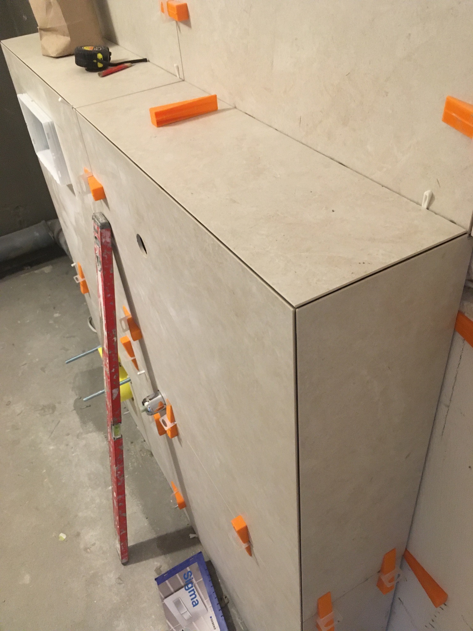 Montaż jasnych płytek na zabudowie w Siemiatyczach, widoczne poziomica, miarka, ołówki i system poziomowania płytek.