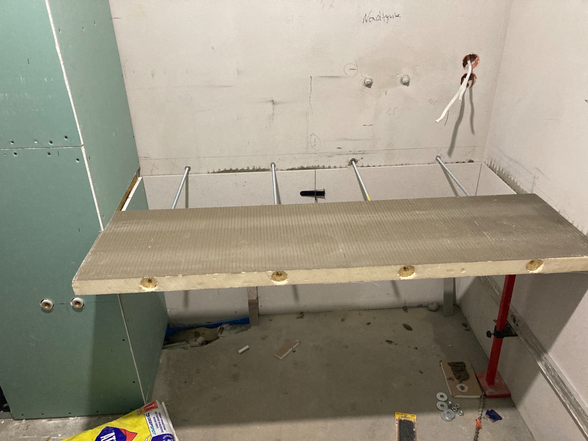 Przygotowanie do montażu płytki ceramicznej na stelażu z metalowymi wspornikami w łazience, widoczne otwory w płycie, ściany przygotowane pod płytki, instalacja elektryczna wyprowadzona.