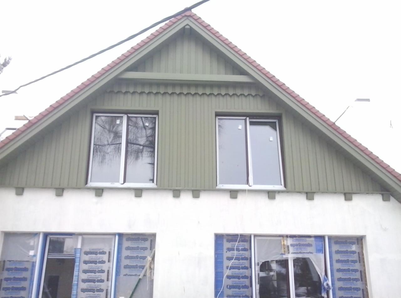 Fasada domu z nowymi oknami na poddaszu i oknami na parterze w trakcie montażu, zabezpieczonymi folią. Zielona drewniana elewacja poddasza i biała ściana parteru.
