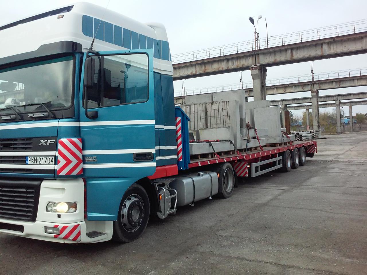 Ciężarówka DAF XF z otwartymi drzwiami, przewożąca prefabrykaty betonowe na naczepie w Ciechocinku, na tle betonowej konstrukcji.