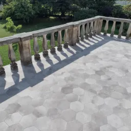 Balkon z szarą, heksagonalną podłogą, kamienna balustrada rzucająca cień, widok na zielony ogród.