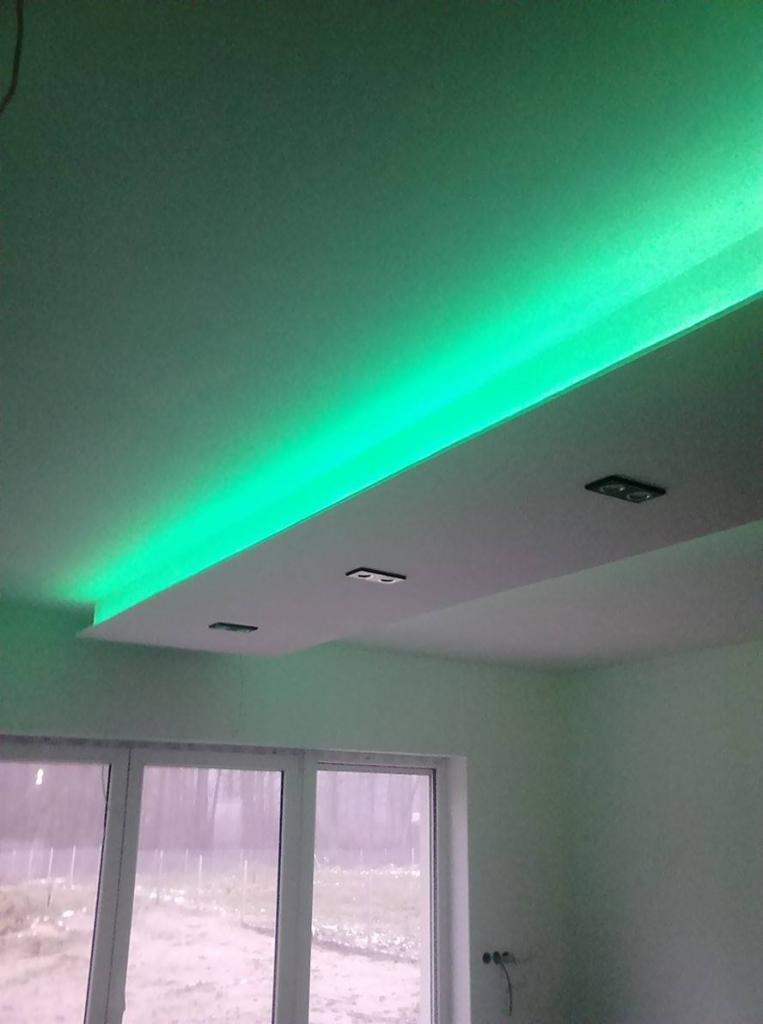 Podwieszany sufit z oświetleniem LED w kolorze zielonym, widok na okno. Nowoczesne wykończenie wnętrza.